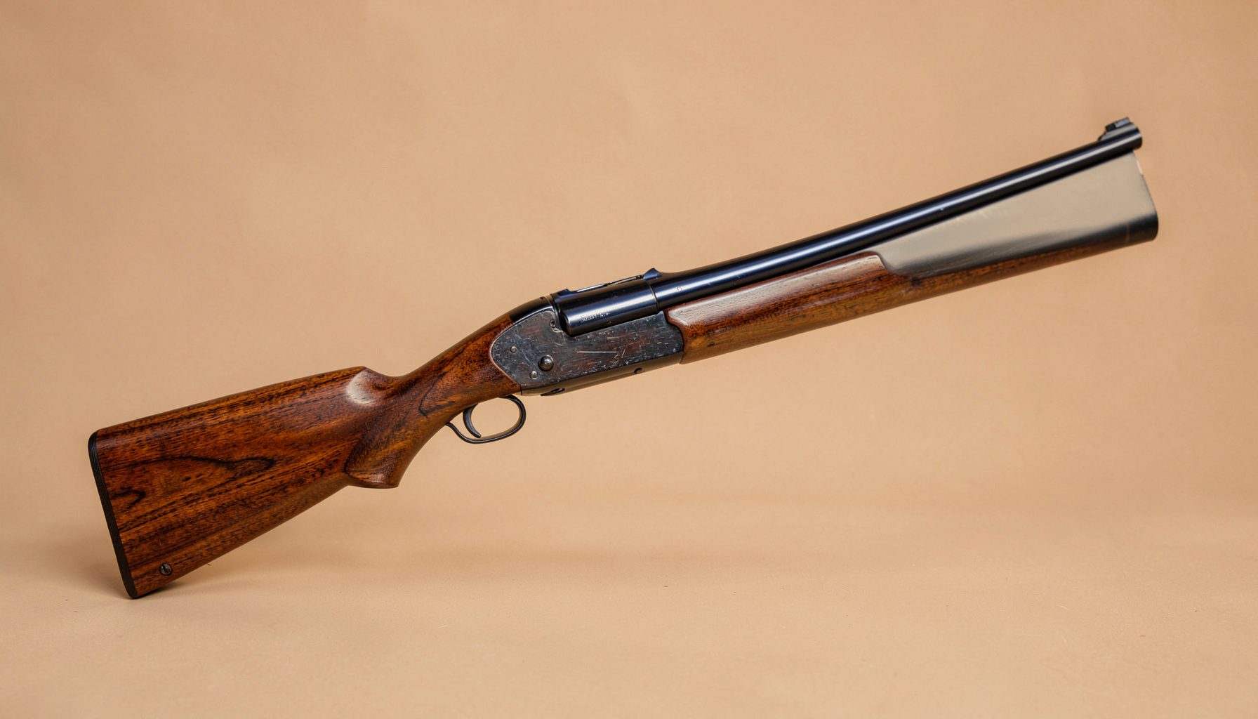A Browning Magnum Twenty 20 gauge shotgun with rich walnut stock and polished blued barrel, shown against a warm neutral backdrop