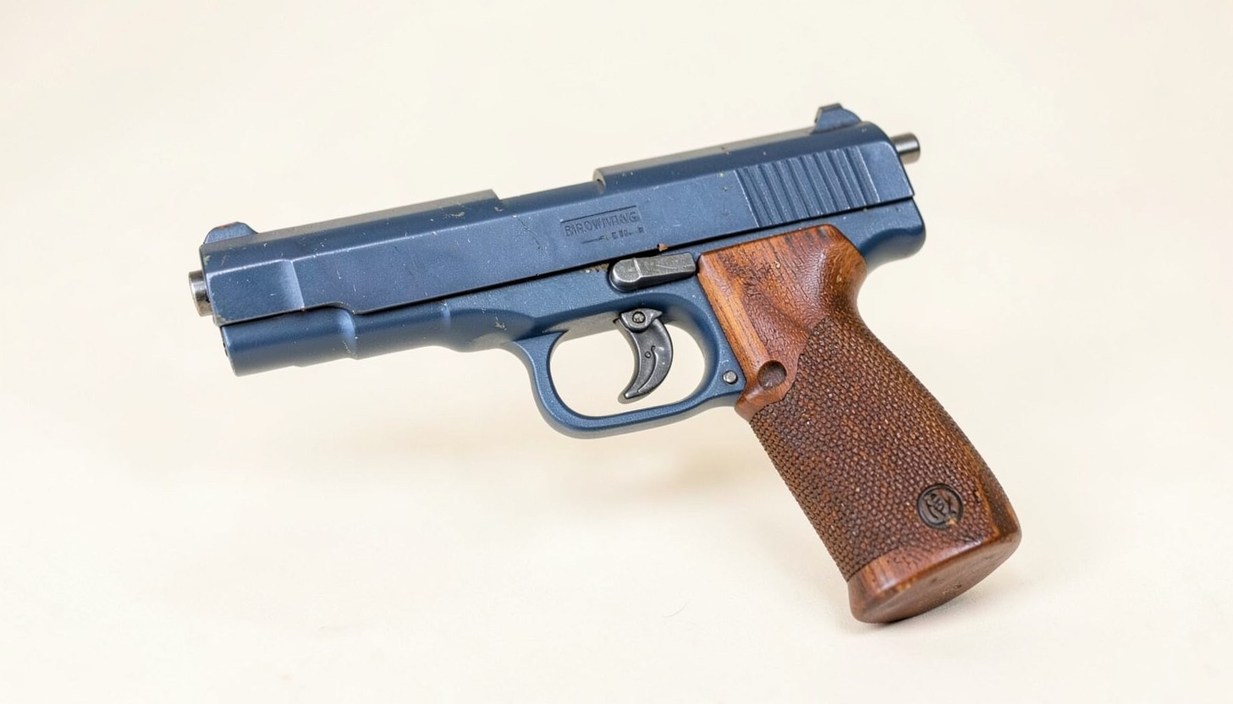 A classic Browning Challenger 22 LR pistol with blued finish and wood grips, shown against a soft off-white backdrop