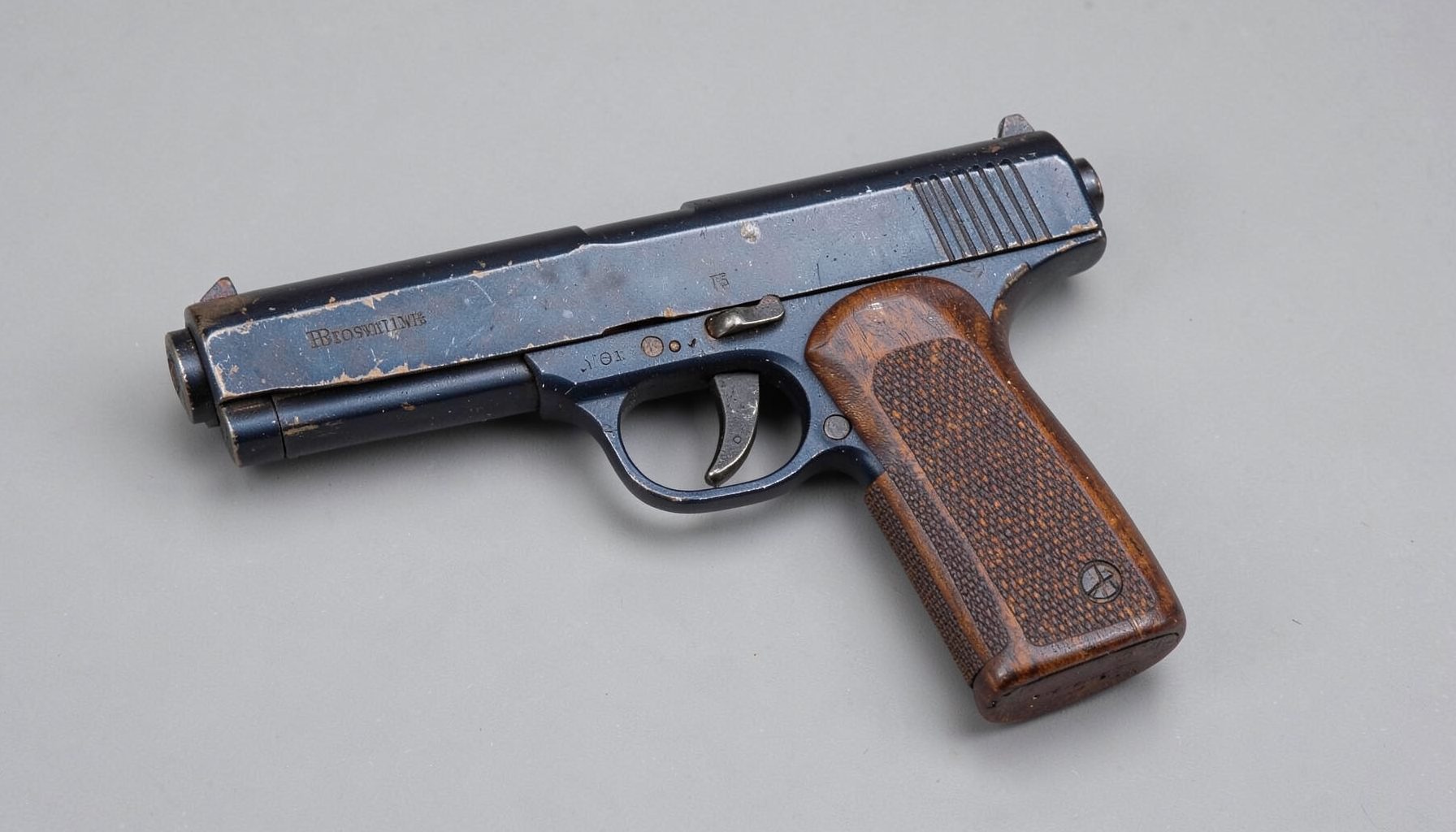 A well-worn Browning Hi-Power pistol with dark blued steel finish and checkered walnut grips, photographed on a neutral gray background